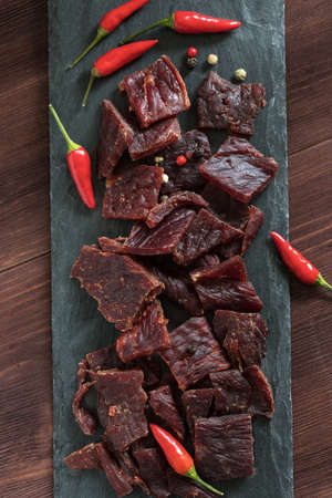 spice beef jerky on black shale board with red peppersの写真素材