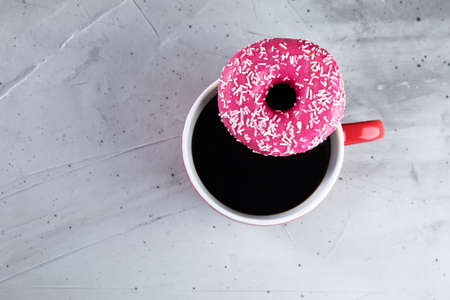 cup of black coffee with pink donut on a cement background