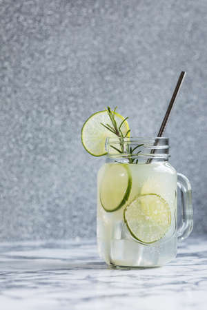 Refreshing drink with lime and lemon slices and rosemary in a glass with metal tube
