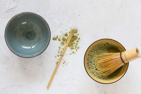 Green tea matcha in one bowl with whisk, empty bowl and between them a spoon with a scattered slide...