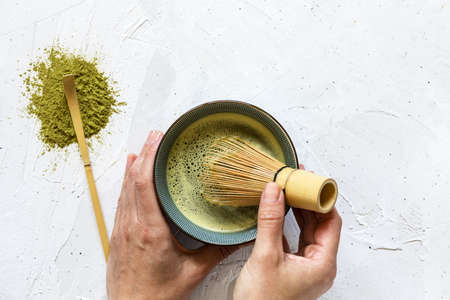 Female hands hold bowl with the green matcha tea and whip it with whiskの写真素材