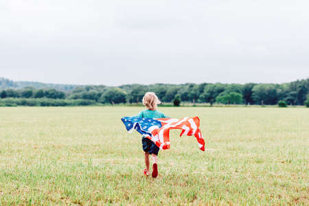 Little boy runs across the field, holds a waving American flagの写真素材
