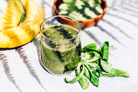 Green smoothie of banana, lettuce and spirulina on light background with shadowsの写真素材