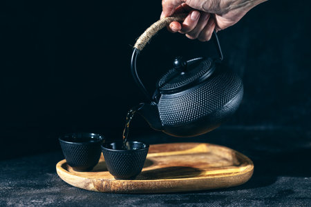 Hand holds a black kettle and pours tea into a mug, low keyの写真素材