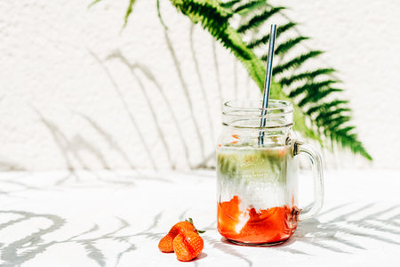 Strawberry matcha latte drink under bright sun and shade from fernの写真素材
