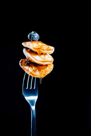 Three mini pancakes on fork, poured with honey, and blueberry on topの写真素材
