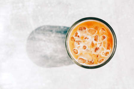 Cold drink of coffee with milk and ice on a white table, top viewの写真素材