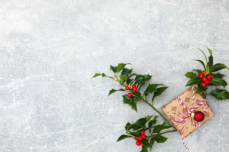 Christmas gift in craft paper, next to three branches of Holly plants with red berries, copy spaceの写真素材