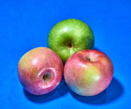 three red and green apples on blue background