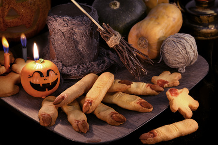 Halloween background with finger cookies and witch magic objects in candle light. Pumpkins, broom stick and warlock hat with traditional sweetsの写真素材
