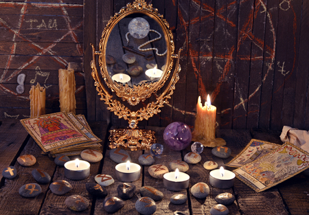 Magic ritual with ancient runes, mirror, tarot cards and candles. Halloween background, black magic rite or spell, occult and esoteric objects on witch tableの写真素材