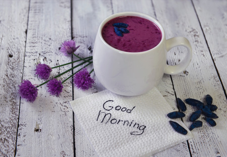 Cup of honey berry smoothie with summer flowers and good morning text on white napkin. Morning still life with healthy breakfast. Beautiful summer vintage background, vegetarian and vegan conceptの写真素材