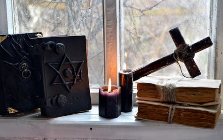 Black magic books, black candles and cross against old window. Occult, esoteric, divination and wicca concept, mystic backgroundの写真素材