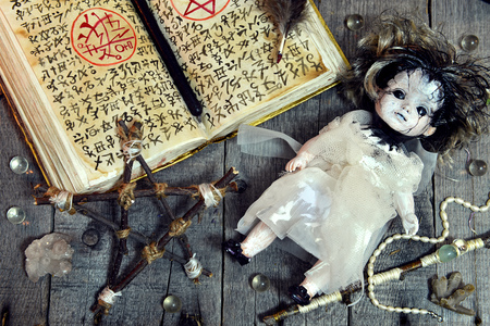 Scary doll, pentagram and open magic book with evil symbols on witch table. Occult, esoteric, divination and wicca concept. No foreign text, all symbols on pages are fantasy, imaginary onesの写真素材