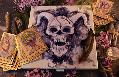 Mystic box with horned demon, tarot cards, magic objects, black candles and lilac flowers. Occult,...