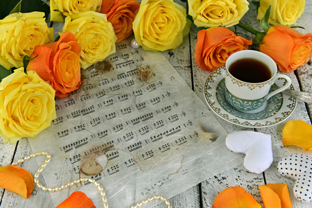 Yellow roses with cup of black tea, heart decorations, pearl necklace and music sheet. Vintage romantic background, retro design with antique objects, birthday card conceptの写真素材