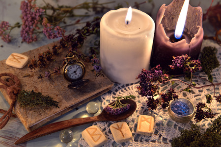 Wooden runes, healing herbs, black and white candles and diary book on lace napkin. Magic ritual. Wicca, esoteric and occult background with vintage witch objectsの写真素材