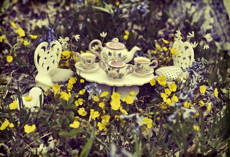 Fairy tea party concept in retro style. Small table and chairs with tiny dishware.  Greeting cards, birthday, love and romantic concept. Vintage summer backgroundの写真素材