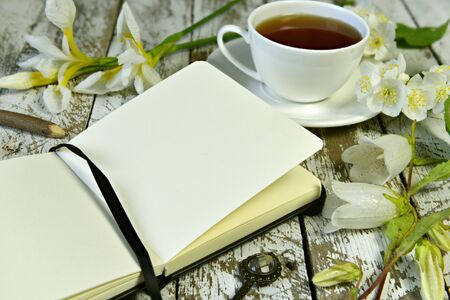 Open diary with copy space pages, cup of tea and flowers on wooden table. Vintage still life, poetry and literature reading conceptの写真素材