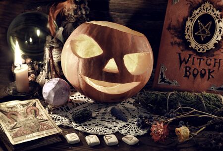 Halloween still life with witch book, Jack O Lantern pumpkin, tarot card and runes. Esoteric, wicca...