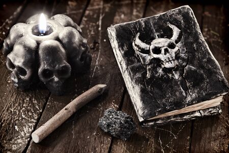 Close up of old book with black magic spells and black candles on witch table. Wicca, esoteric and occult background with vintage magic objects for mystic rituals. Halloween and gothic conceptの写真素材
