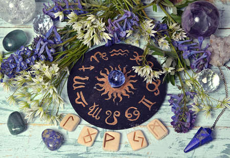 Still life with black zodiac circle, runes, crystal and flowers on witch altar table.  Esoteric,...