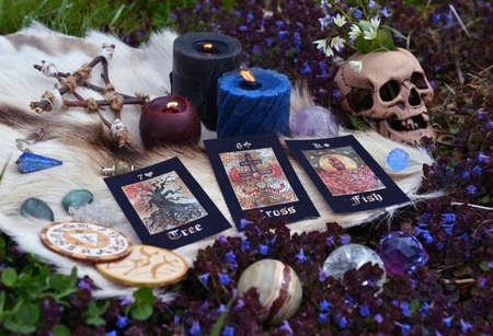 Beltane ritual with tarot cards, skull, burning candles, pentagram and crystals outside. Esoteric,...