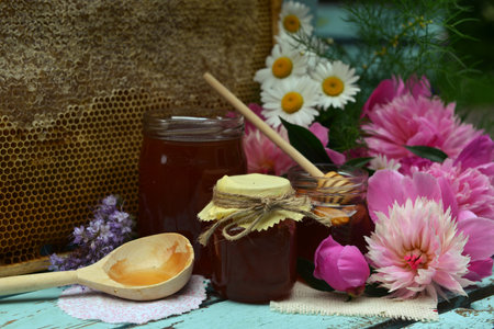 Still life with natural honey in jar, dipper, flowers and stick on wooden background outside....