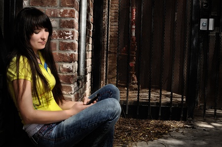 girl sitting by the door in a brick steps and metal door in backgroundの写真素材