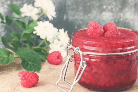 Glass jar with raspberry jam . Homemade preserved and with fresh raspberry, leaf on wooden table