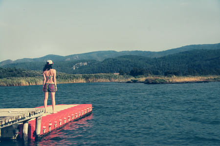 One beautiful sport girl standing with her back on the pontoon looking out into the distance at sea and on the mountains. lifestyleの写真素材