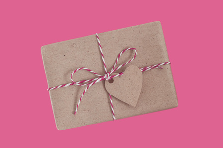 Gift wrapped on a craft paper and decorated heart on the pink backgroundの写真素材
