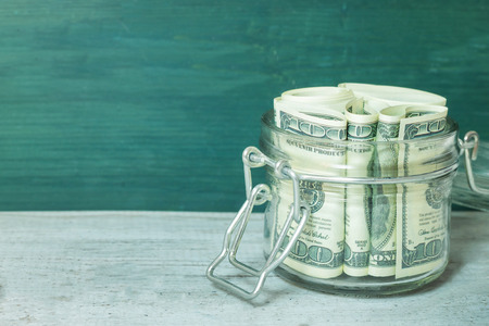 Dollar bills in glass jar on wooden table. Saving money concept.の写真素材
