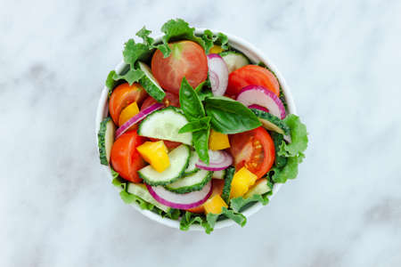 Green salad with tomato and fresh vegetables isolated on gray background. Top view - vegetarian foodの写真素材
