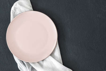 Empty pink plate on black table and napkin. Food background for menu, recipe. Table setting. Flatlay, top view. Mockup for restaurant dishの写真素材