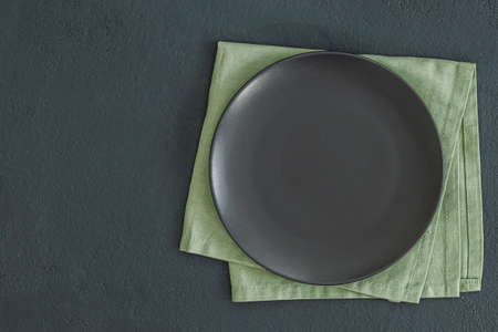 Empty black slate plate on dark stone table and napkin. Food background for menu, recipe. Table setting. Flatlay, top view. Mockup for restaurant dishの写真素材
