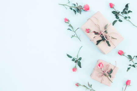 Gift or present box wrapped in craft paper and rose flower on blue table top view. Flat lay styling....