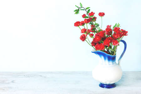 Roses in white vase on wood table on blue wall with copy space. Greeting card for mother ot woman dayの写真素材