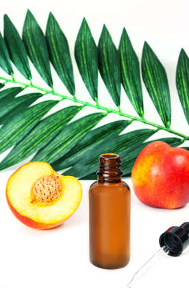 Bottle of peach oil, decorated with peaches on wooden table and dark borwn background. The concept of an aroma oil, the ingredients of an aroma oil, or aromatherapy.の写真素材