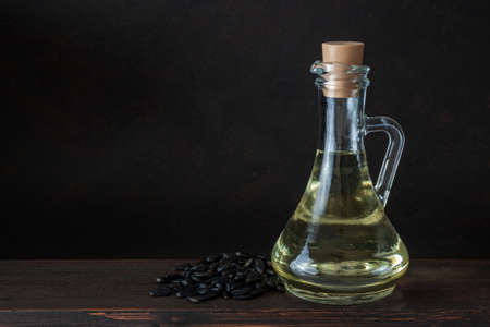 Bottle or jar of sunflower oil on wooden table over dark brown background empty space for text....