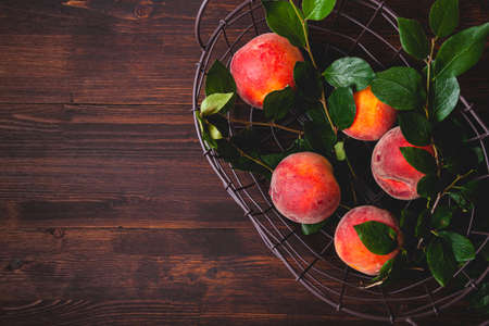 Peach or nectarine in wicker basket with leaf on wooden background. Fruit backgroundの写真素材