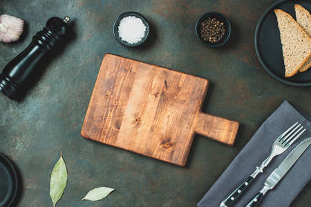 Chopping board, seasonings and rosemary on dark background. Cutting board for menu Top view. Food...