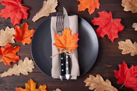 Empty black plate with autumn maple, oak leaves on brown wooden table. Backgroud for restaurant...