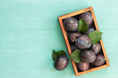 Freash plums in wooden box on wood table top view. Blue pulm with leaves. Food fruit backgroundの写真素材