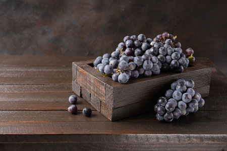 Bunch of black grapes in wooden box on dark wooden background.の写真素材