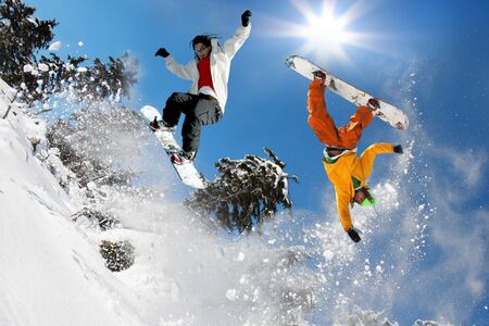 Snowboarders jumping against blue skyの写真素材