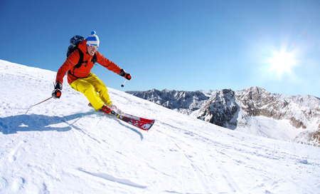 Skier skiing downhill in high mountains against sunsetの写真素材