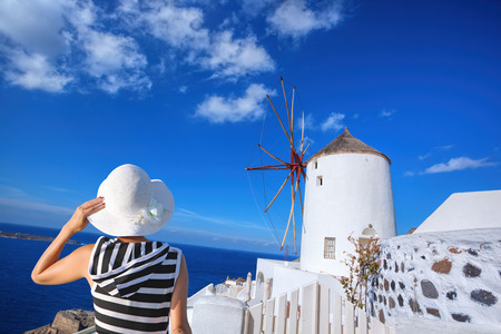 Woman holding a hat against windmill in Oia village on Santorini island, Greeceの写真素材