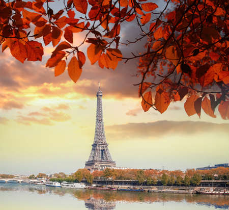 Eiffel Tower with autumn leaves against colorful sunset in Paris, France