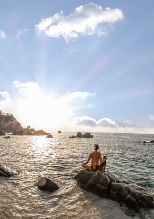 Girl with dog sitting on a rock next to the beach and meditating against sunset over the sea. Calabria paradise in Italyの写真素材